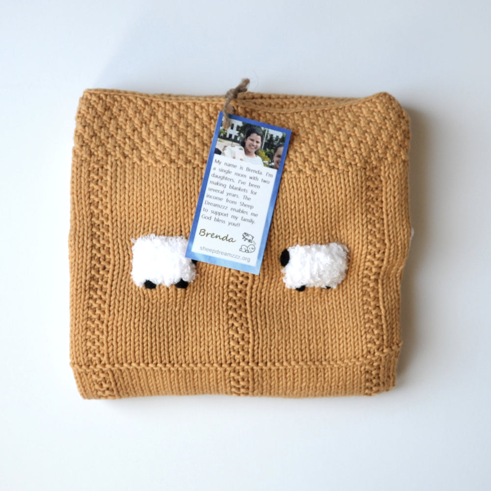 Coffee Milk color hand-knitted baby blanket, folded, with a tag showing who knitted it.