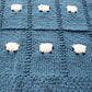 100% organic cotton baby blanket, hand-knitted. This is a close-up shot at an angle showing the fine knitting and organic cotton sheep.
