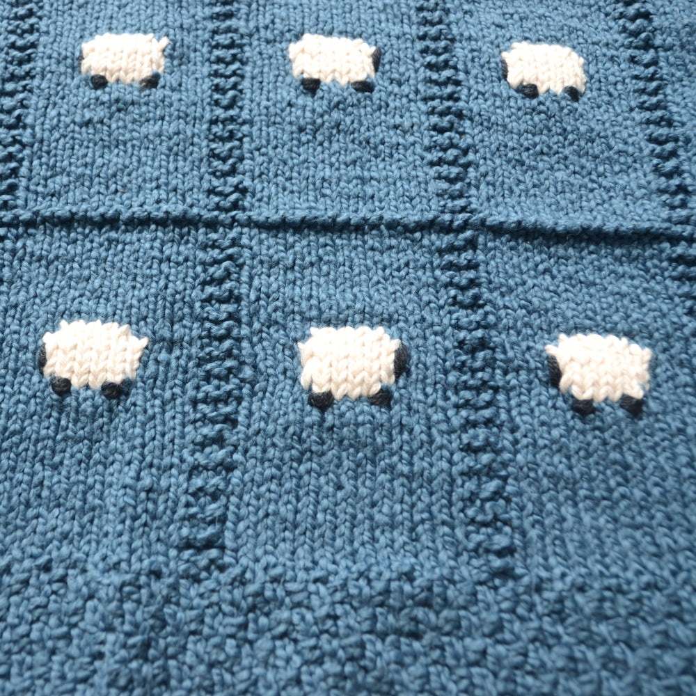 100% organic cotton baby blanket, hand-knitted. This is a close-up shot at an angle showing the fine knitting and organic cotton sheep.