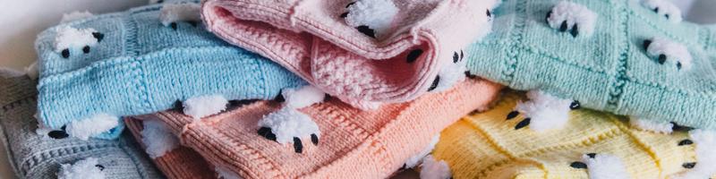 Soft, beautiful, handmade baby blankets of various pastel colors loosely stacked.