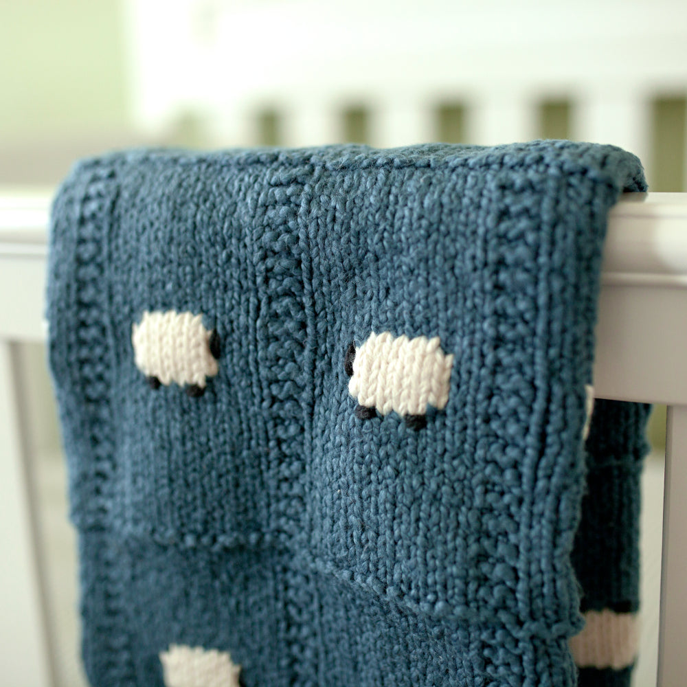 Cadet blue organic cotton baby blanket hanging on the side of a crib
