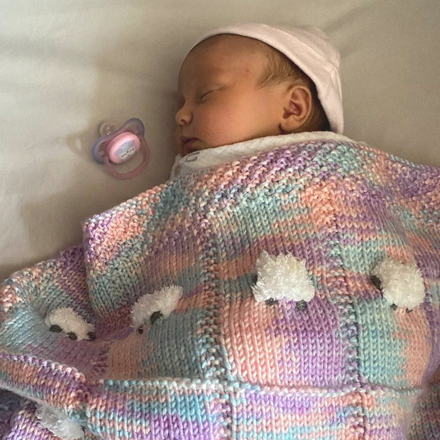 Multicolor baby blanket with pink, lavender, and aqua colors over a young baby.