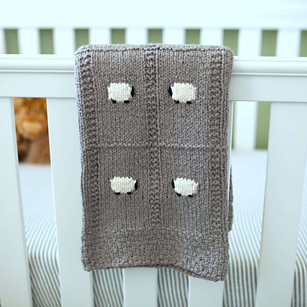All-cotton gray organic baby blanket hanging on the side of a crib