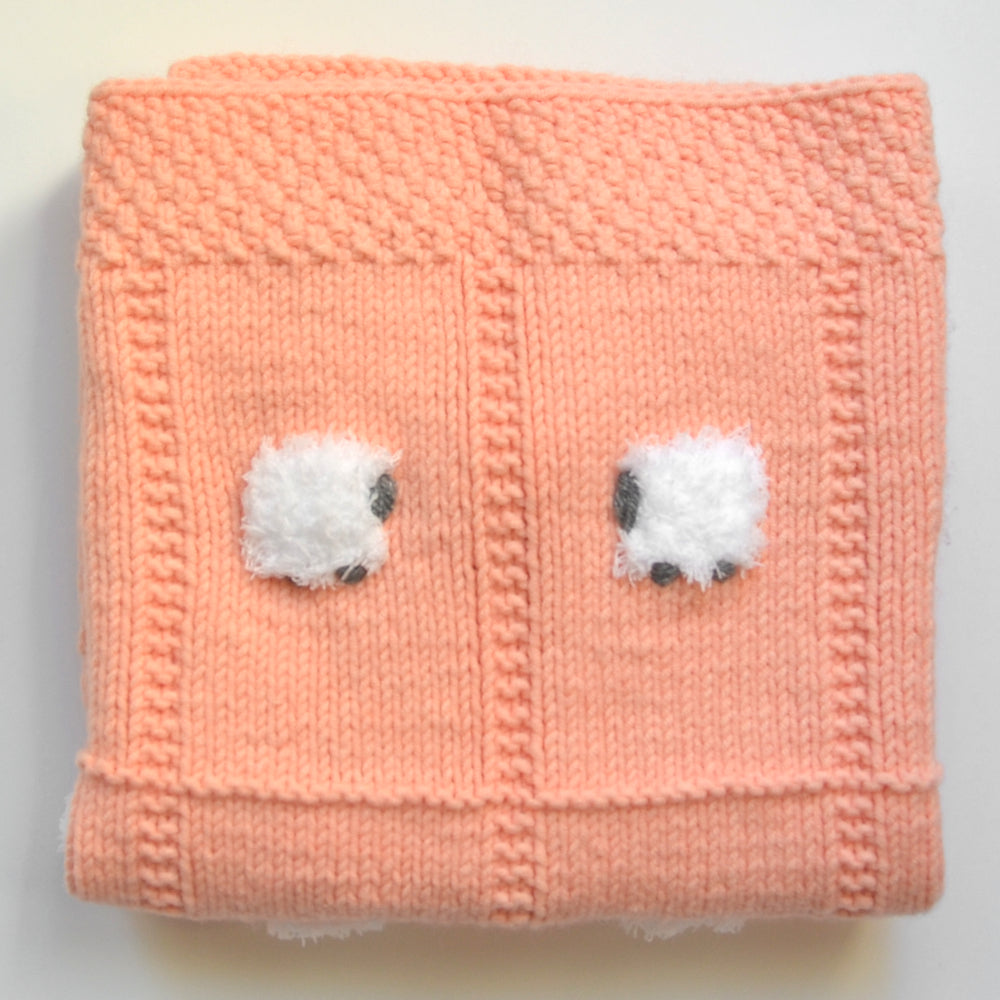 Folded peach baby blanket with 2 fluffy sheep and a tag saying who made it.