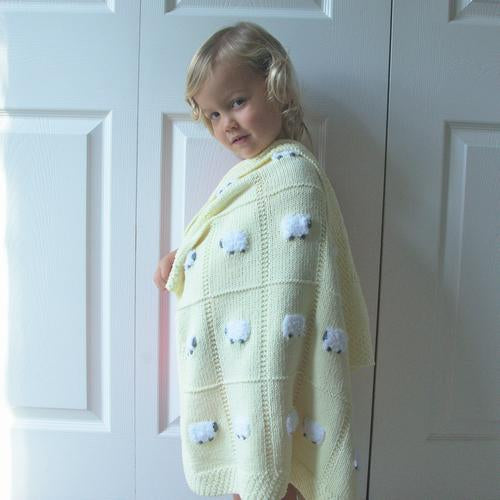 Little girl draped in a pastel yellow hand-knitted baby blanket with 24 fluffy white sheep.
