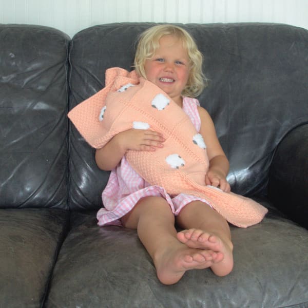 Young girl on a couch hugging a peach-colored baby blanket with fluffy white sheep
