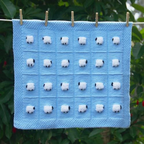 Baby blue baby blanket with sheep on it hanging outside with clothespins
