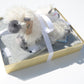 Baby blanket gift set box with clear lid, blanket and lovey inside, and a fluffy sheep doll on top, all tied together with a silky ribbon.