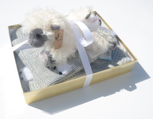 Baby blanket gift set box with clear lid, blanket and lovey inside, and a fluffy sheep doll on top, all tied together with a silky ribbon.