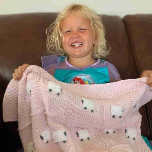 Toddler girl happy with her powder pink handmade baby blanket with 24 fluffy white sheep