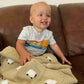 Baby boy enjoying his barley-colored handmade baby blanket with 24 fluffy white sheep