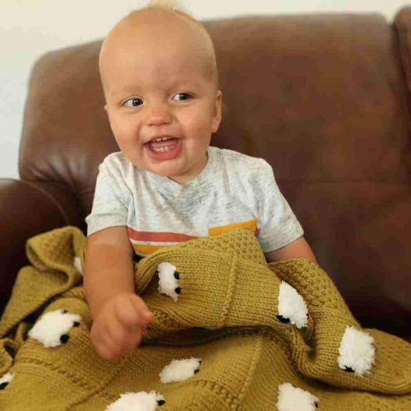Young baby boy laughing with his olive gold handmade baby blanket with 24 fluffy white sheep