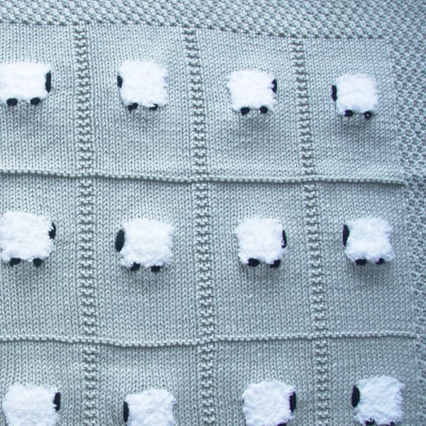 Mostly cotton hand-knitted baby blanket with 24 fluffy white sheep. The color of the blanket is platinum gray.