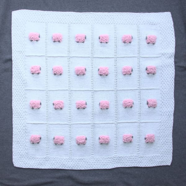 Mostly cotton hand-knitted baby blanket with 24 fluffy pink sheep. The color of the blanket is white.