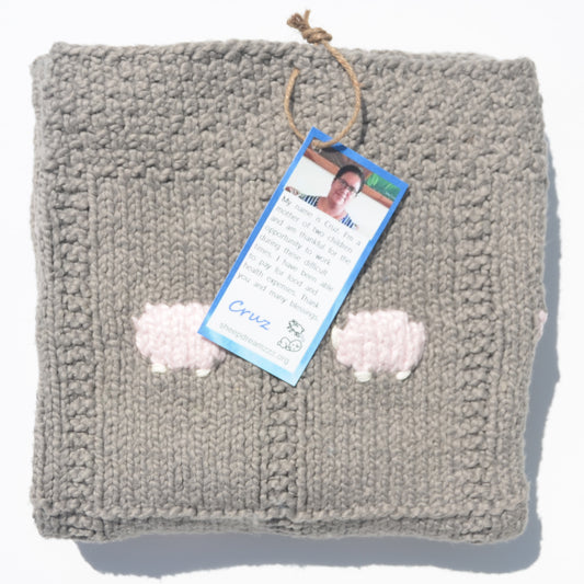 Hand-knitted gray organic cotton blanket, folded, with pale pink sheep that are knitted in showing.