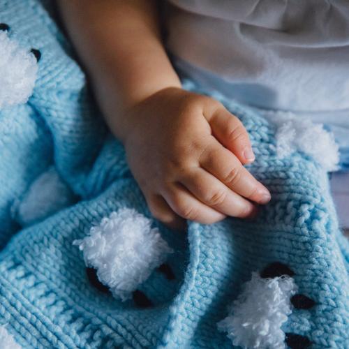 Child's hand resting on top of a blue baby blanket.