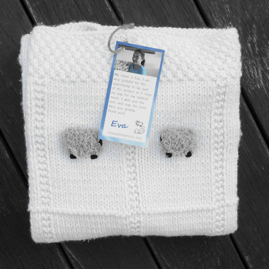 A white hand-knitted baby blanket with fluffy gray sheep on it.